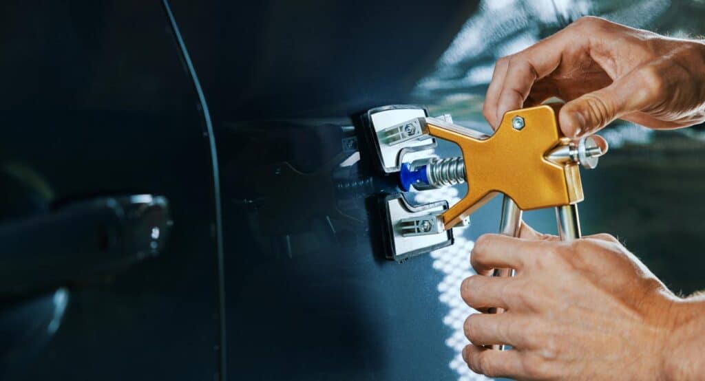 Mechanic uses a paintless dent repair tool to fix a car's dent in Delray Beach, FL