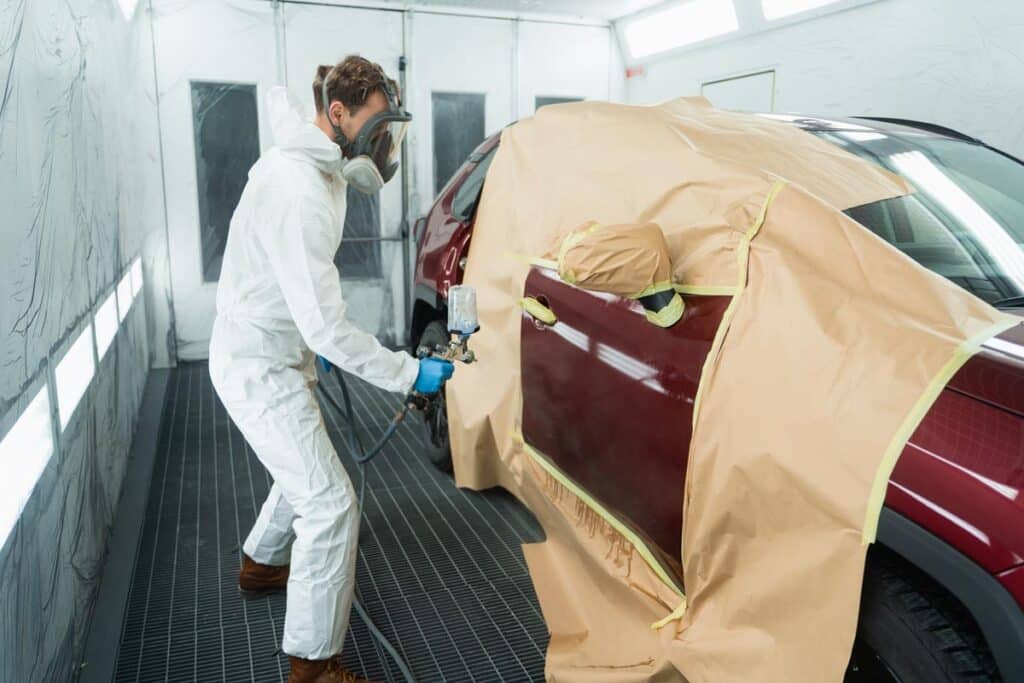 A car technician painting a car at an auto body shop
