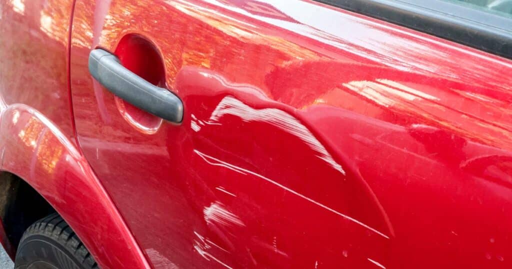 A red automobile with scratches and a dent
