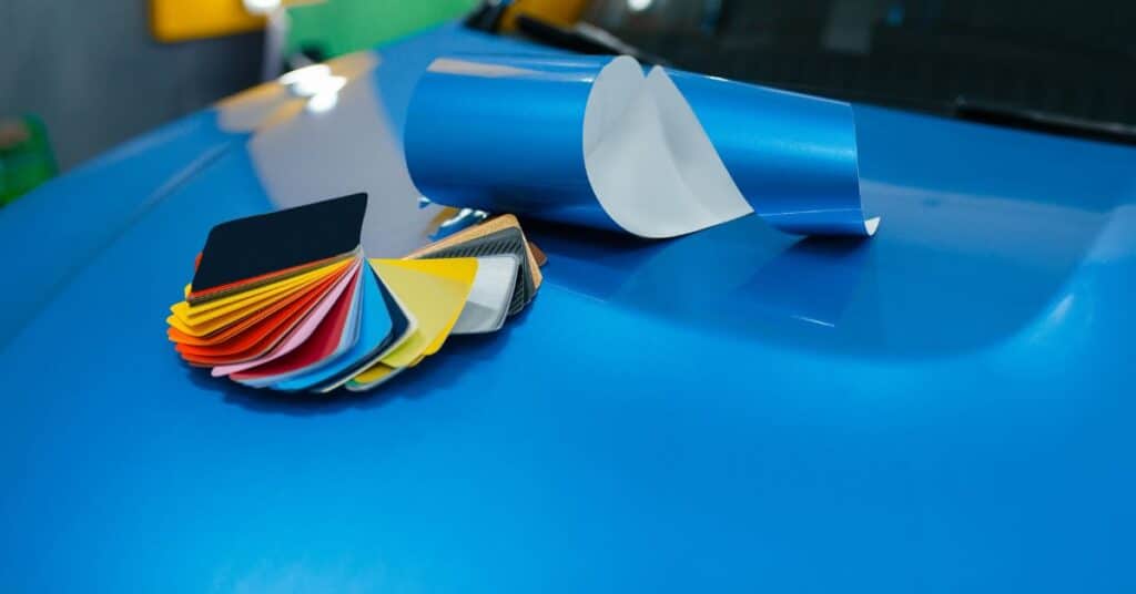 Color sample cards and a blue vinyl sheet placed on a car hood during an auto paint matching process.