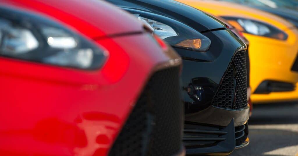 Close-up view of multiple cars in different colors parked side by side, highlighting paint finish differences.