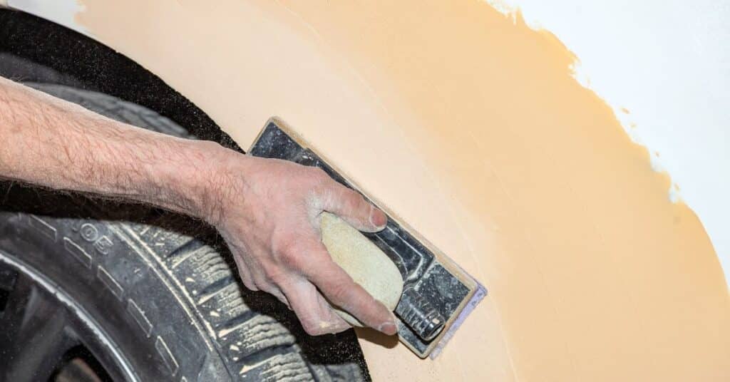 Auto body technician sanding vehicle surface during paint preparation process