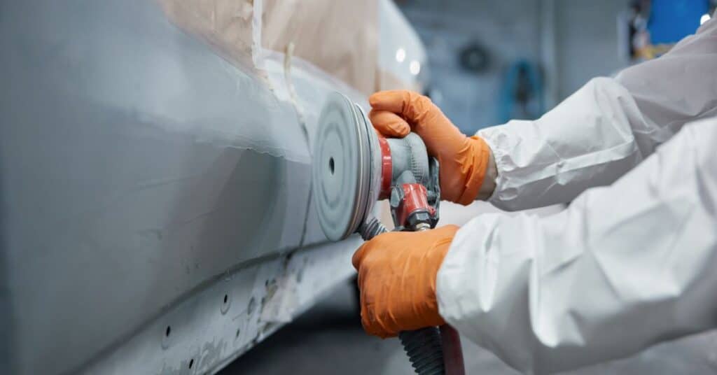 Technician sanding vehicle panel during quality collision repair process