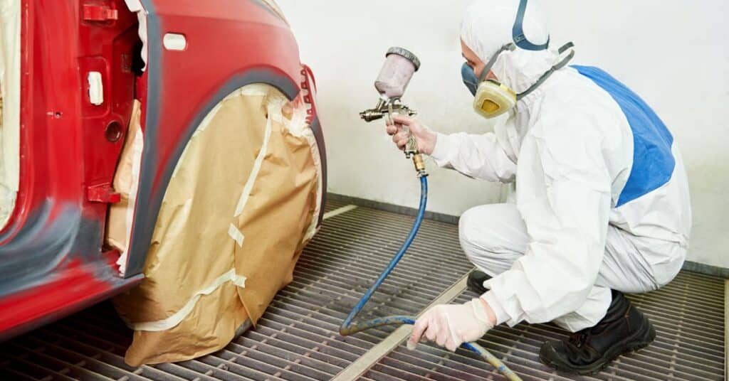 Technician spray painting a vehicle during professional auto body repair.